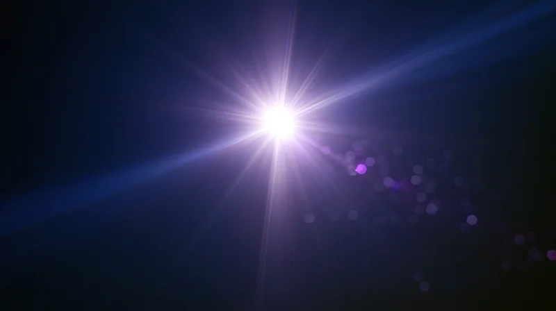 Bright starburst light radiating in dark blue sky with purple bokeh and lens flare effects