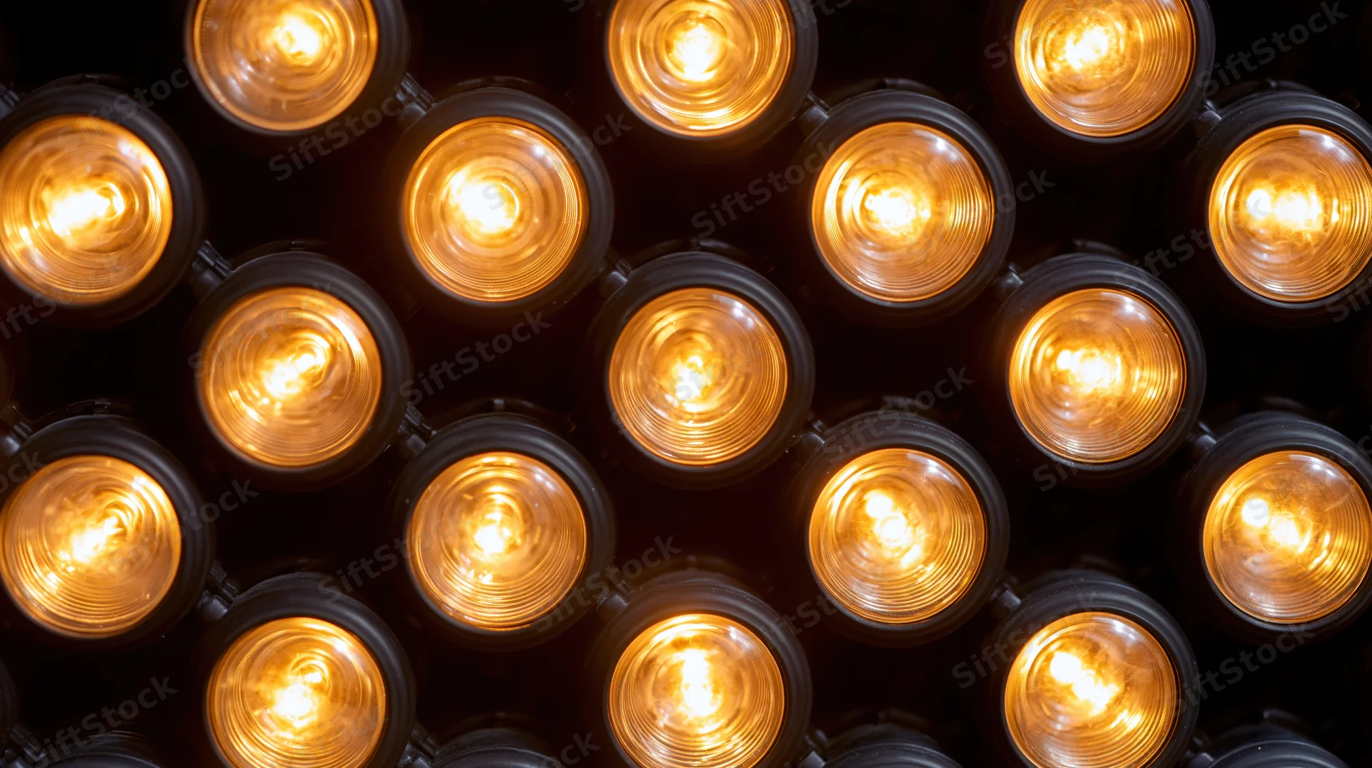 Grid of illuminated warm amber lightbulbs arranged in a repeating pattern on a dark surface
