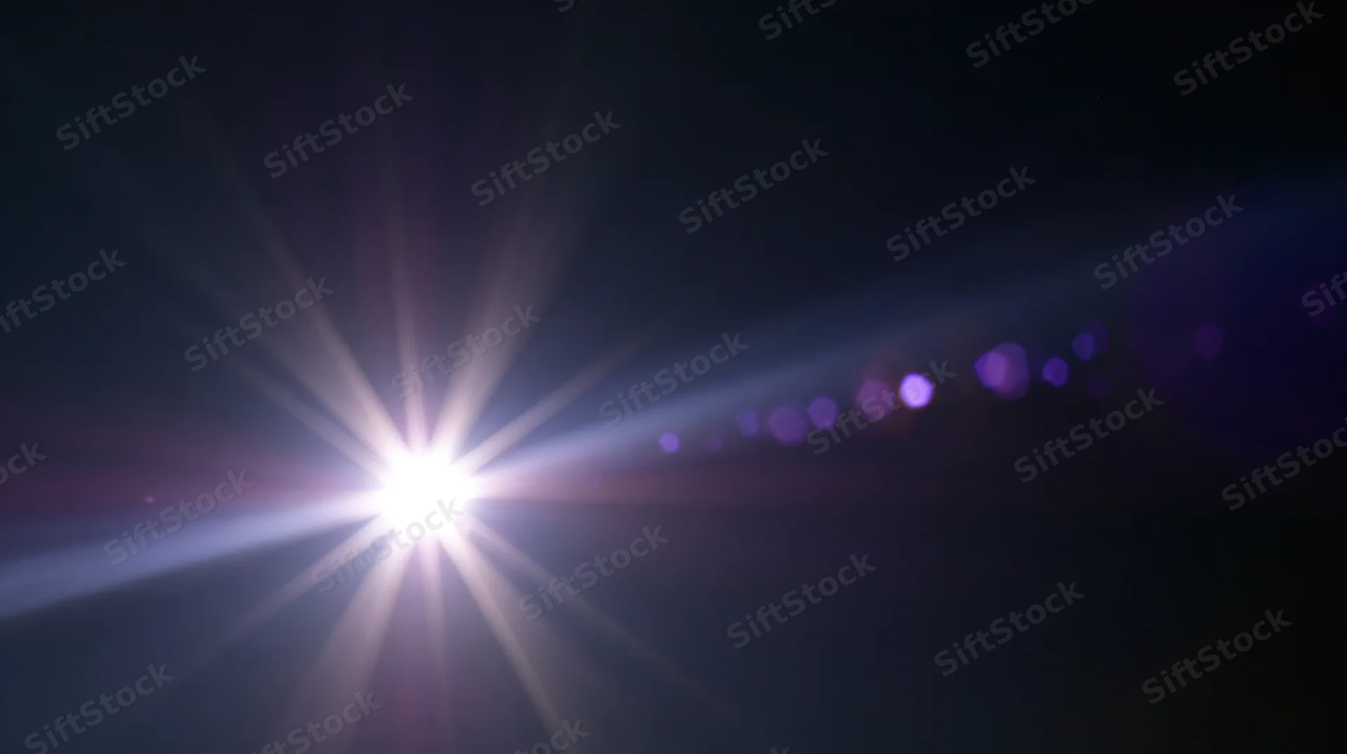 Bright light source emitting starburst flare and purple bokeh against dark background