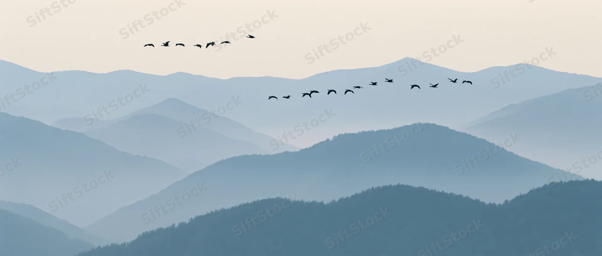 Geese flying in formation over layered misty mountains