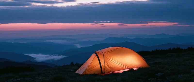 Glowing tent on mountain ridge at twilight overlooking layered valleys and distant peaks