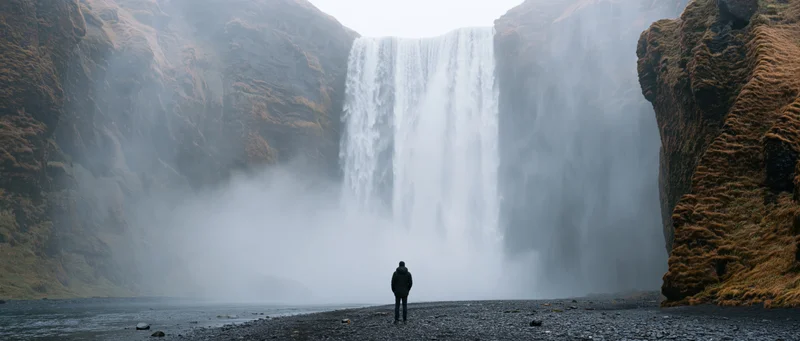 Person standing before a large waterfall in a misty rocky landscape