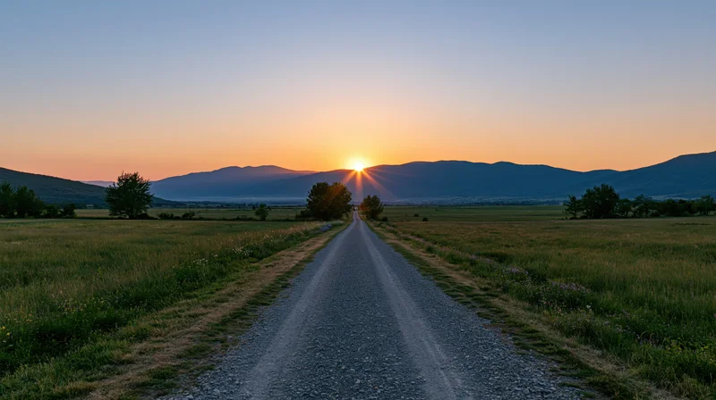 Gravel road stretching toward sunset over mountains in a rural field
