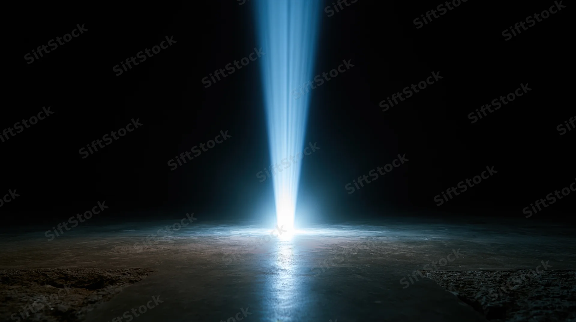 A vertical blue light beam shining down onto a dark concrete floor, creating a glowing reflection in the center