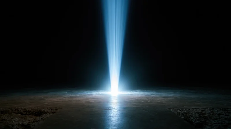 A vertical blue light beam shining down onto a dark concrete floor, creating a glowing reflection in the center