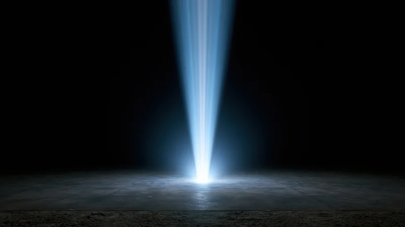 Vertical blue light beam shining down on dark concrete floor in empty studio space