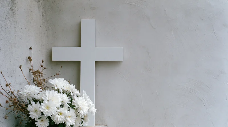 White cross with white chrysanthemums arranged at its base against a concrete wall