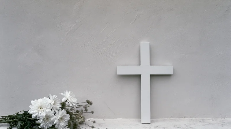 White cross standing beside a bouquet of white chrysanthemums on a concrete wall in a cemetery