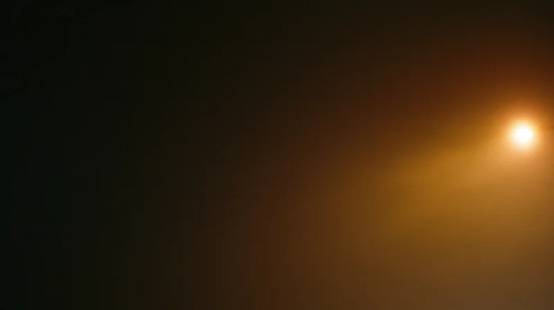 A glowing streetlight casting warm light in a dark foggy urban night scene with soft haze and copyspace