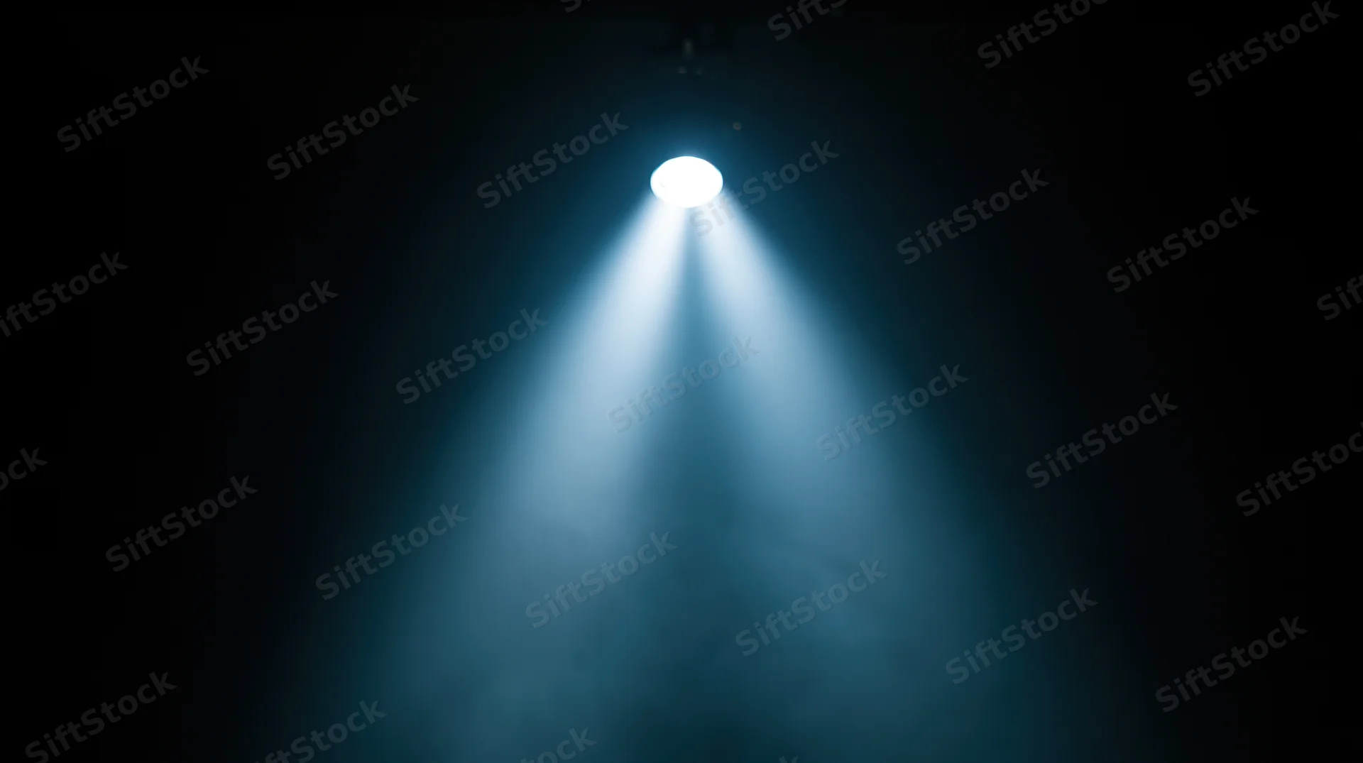 Spotlight beam shining down on dark stage with blue haze