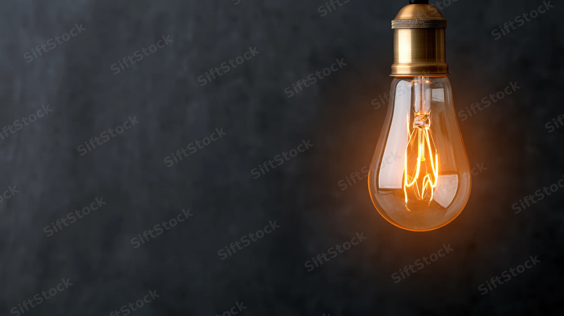 Glowing vintage incandescent lightbulb hanging against dark textured background with copyspace