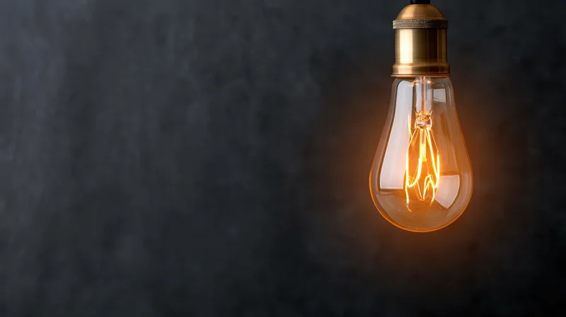 Glowing vintage incandescent lightbulb hanging against dark textured background with copyspace