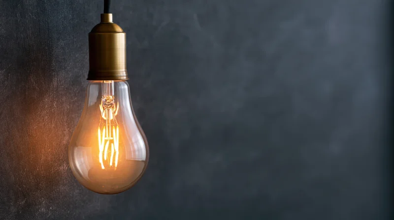 Glowing vintage incandescent lightbulb hanging against dark textured wall with copyspace