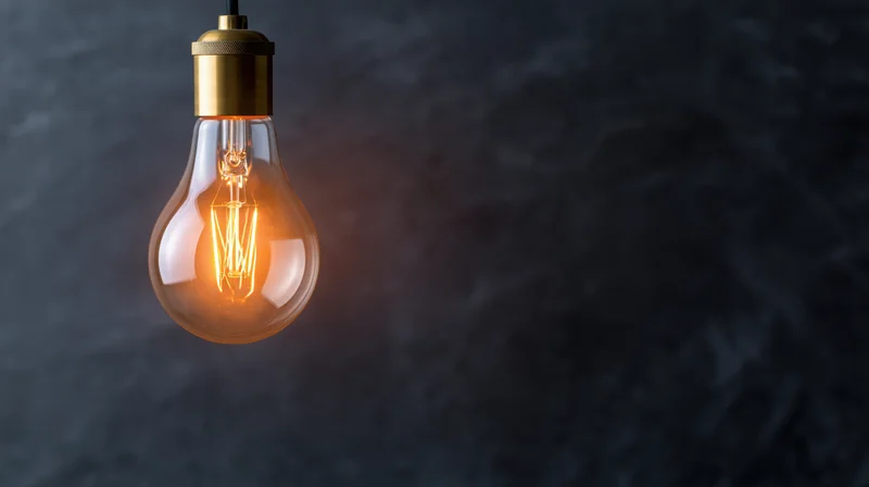 Vintage lightbulb glowing warmly while hanging from a ceiling against a dark textured background