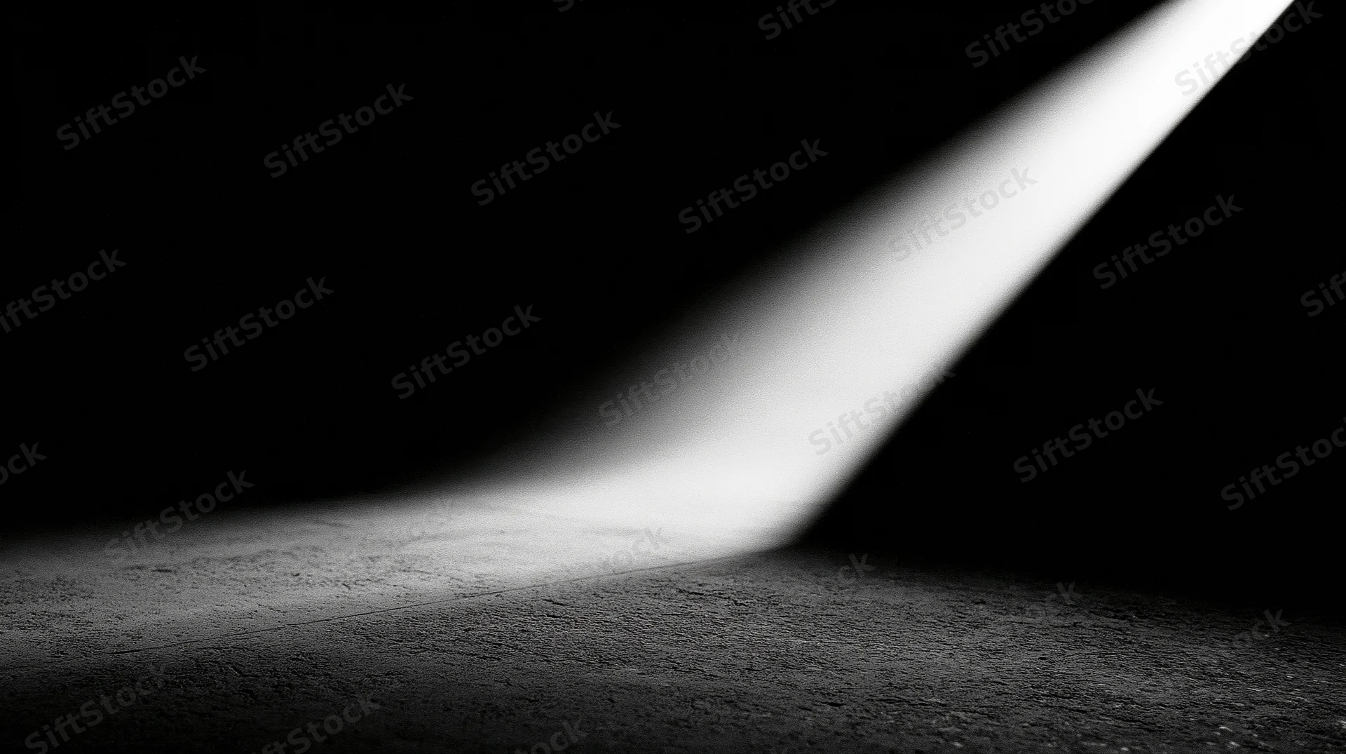 A diagonal beam of light illuminates a textured concrete floor in a dark space