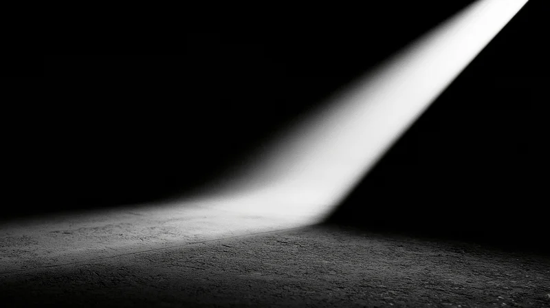 A diagonal beam of light illuminates a textured concrete floor in a dark space