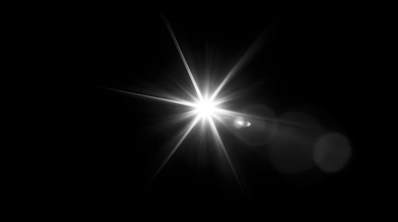 Bright starburst light flare against black background with bokeh highlights and copyspace