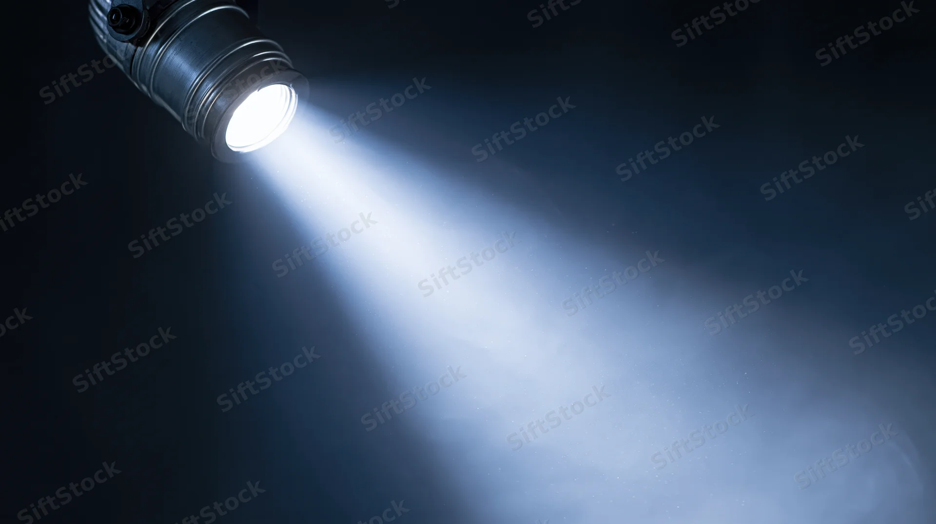 Spotlight casting a bright beam of light into dark space with visible haze