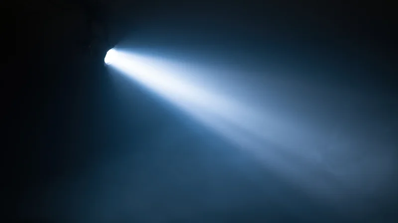 Bright spotlight beam cutting through dark smoky stage atmosphere