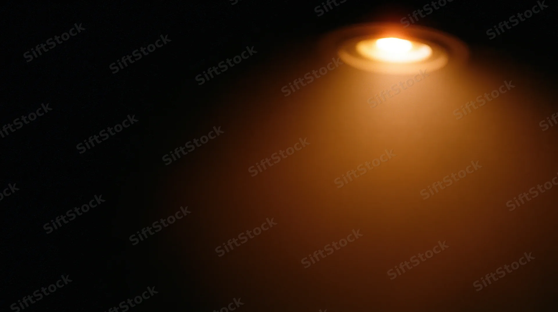 Warm recessed ceiling light glowing in dark indoor space with soft beam and shadow