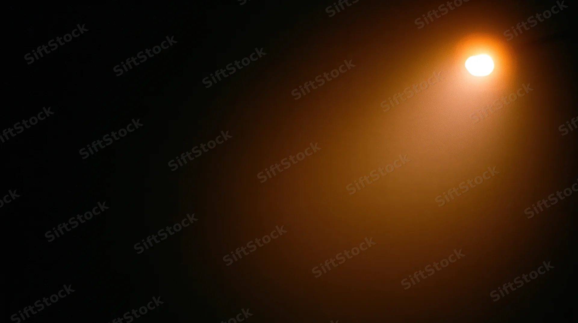 A glowing lightbulb casting warm orange illumination in a dark night setting with soft haze and copyspace