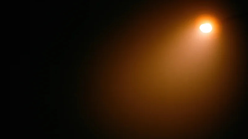 A glowing lightbulb casting warm orange illumination in a dark night setting with soft haze and copyspace