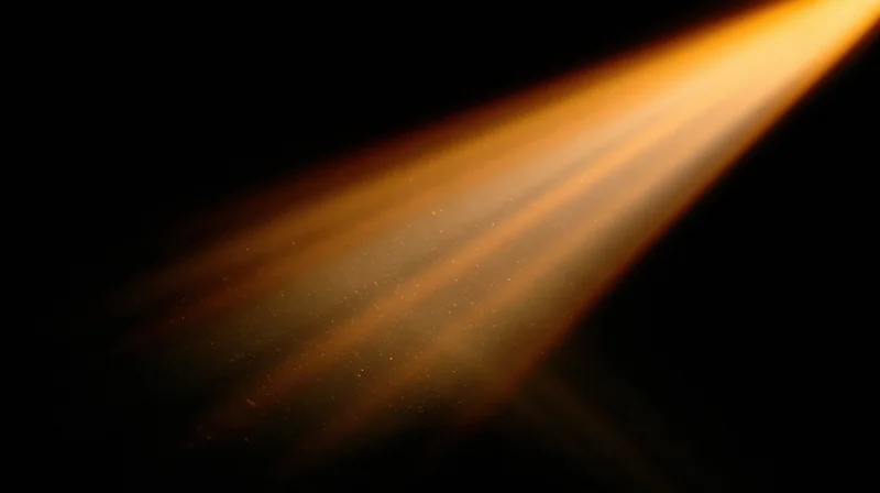 Diagonal beam of warm golden light cutting through dark space with visible dust particles in air
