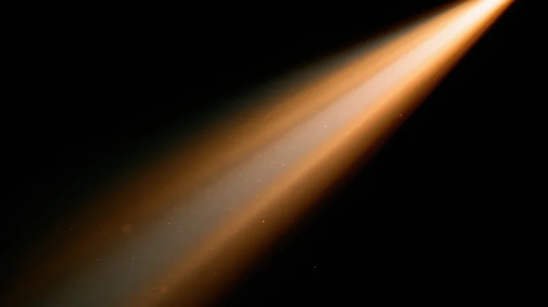 Diagonal beam of warm orange light radiating across dark space with floating particles