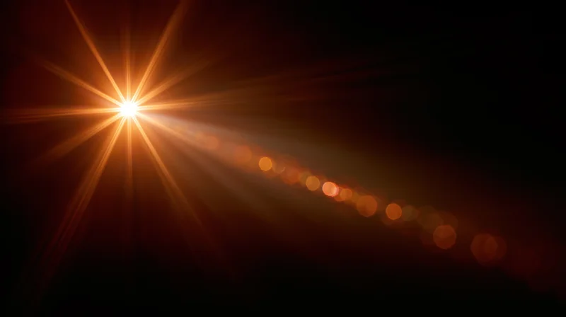 Bright orange starburst light flare with soft bokeh glow on dark background