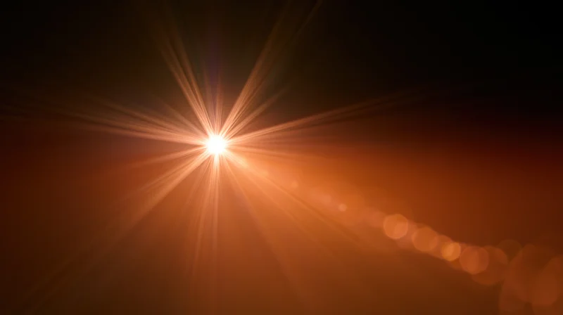 Bright starburst light with radiating rays and bokeh glow on dark orange background