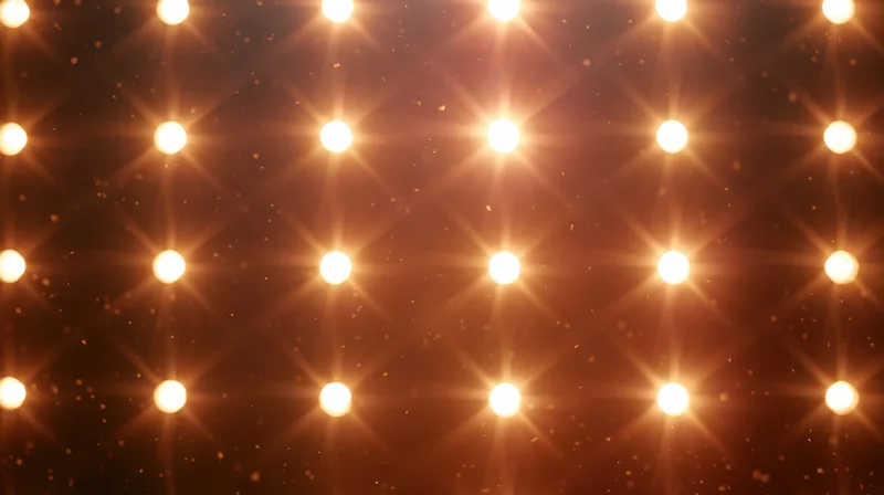 Grid of warm glowing stage lights arranged in rows against a dark background with sparkling particles