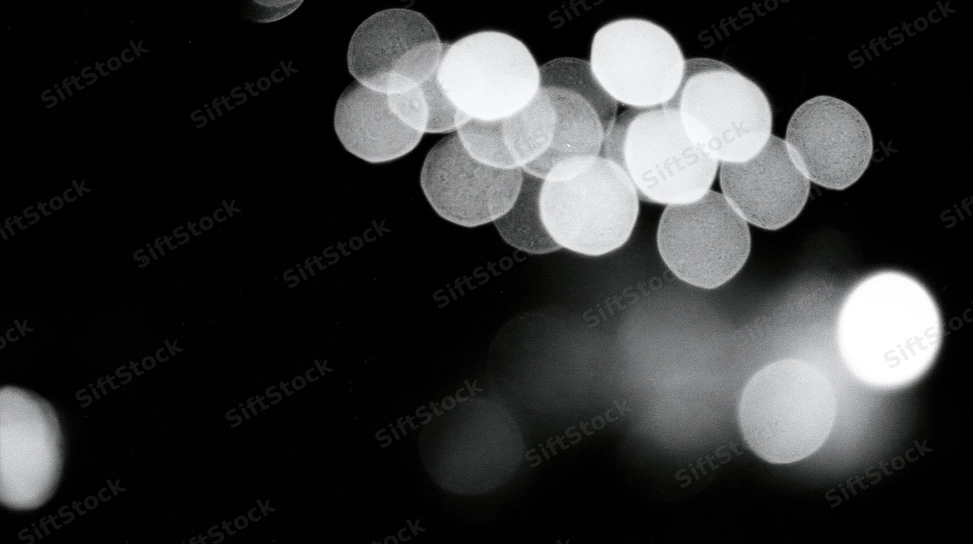 Blurred circular lights glowing against a dark background in monochrome