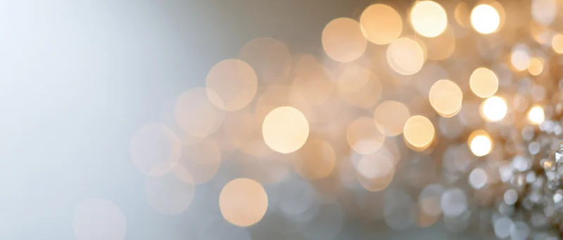 Blurred golden bokeh lights arranged diagonally across a soft background with copyspace on the left