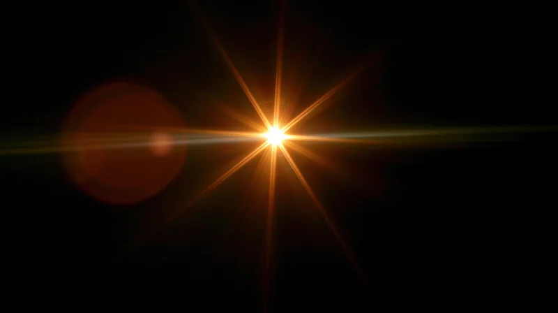 Bright orange starburst light flare on black background with lens flare effect
