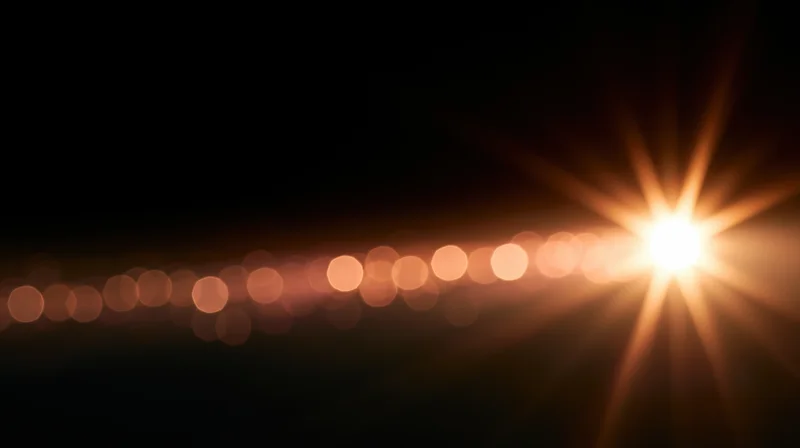 Horizontal line of warm bokeh lights with a bright starburst flare on a dark background