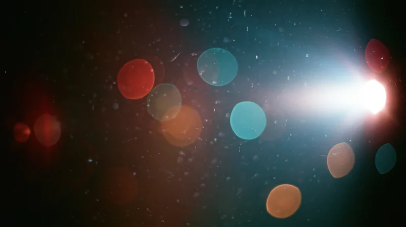 Blurred circular lights in various colors floating in dark space with bright lens flare on right side