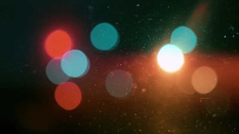 Blurred circular lights in warm and cool tones against a dark background with visible dust particles and lens flare