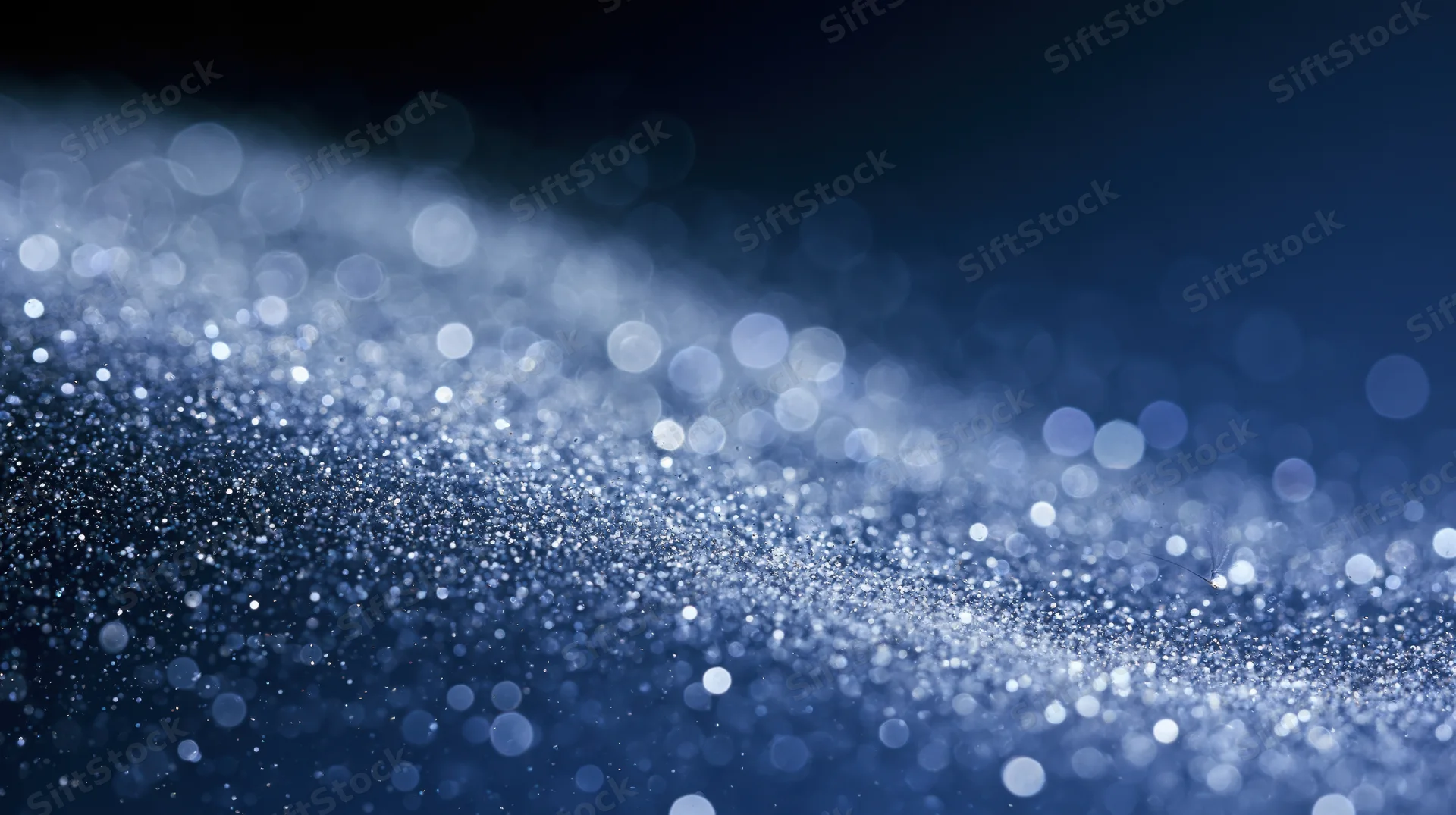 Abstract blue bokeh lights with sparkling glitter particles on dark background