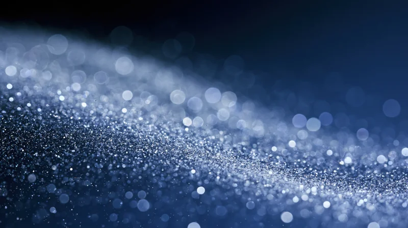 Abstract blue bokeh lights with sparkling glitter particles on dark background