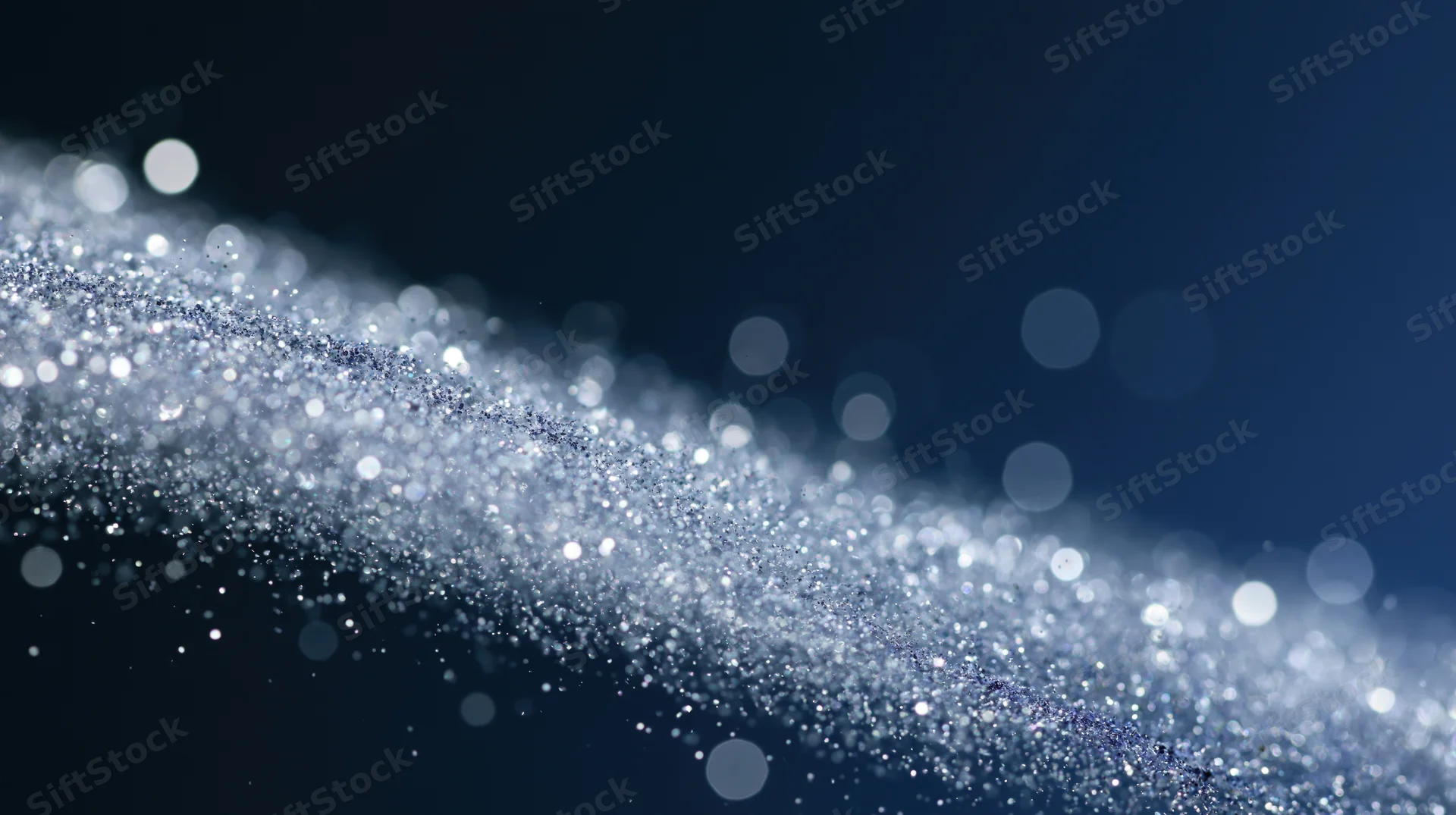 Shimmering silver glitter particles in motion against a dark blue background with bokeh lights