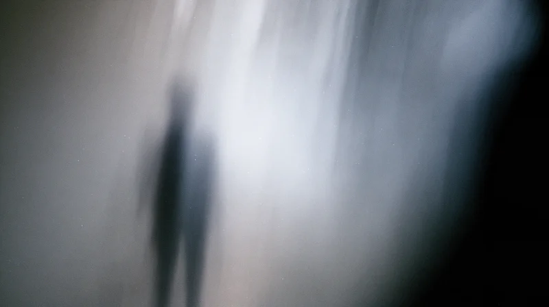 Blurred silhouette of a human figure in foggy light with soft glow and hazy atmosphere