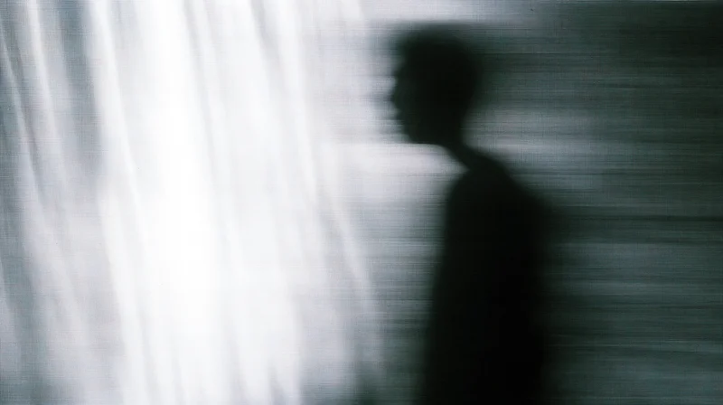 Blurred silhouette of a man in profile against a bright window curtain