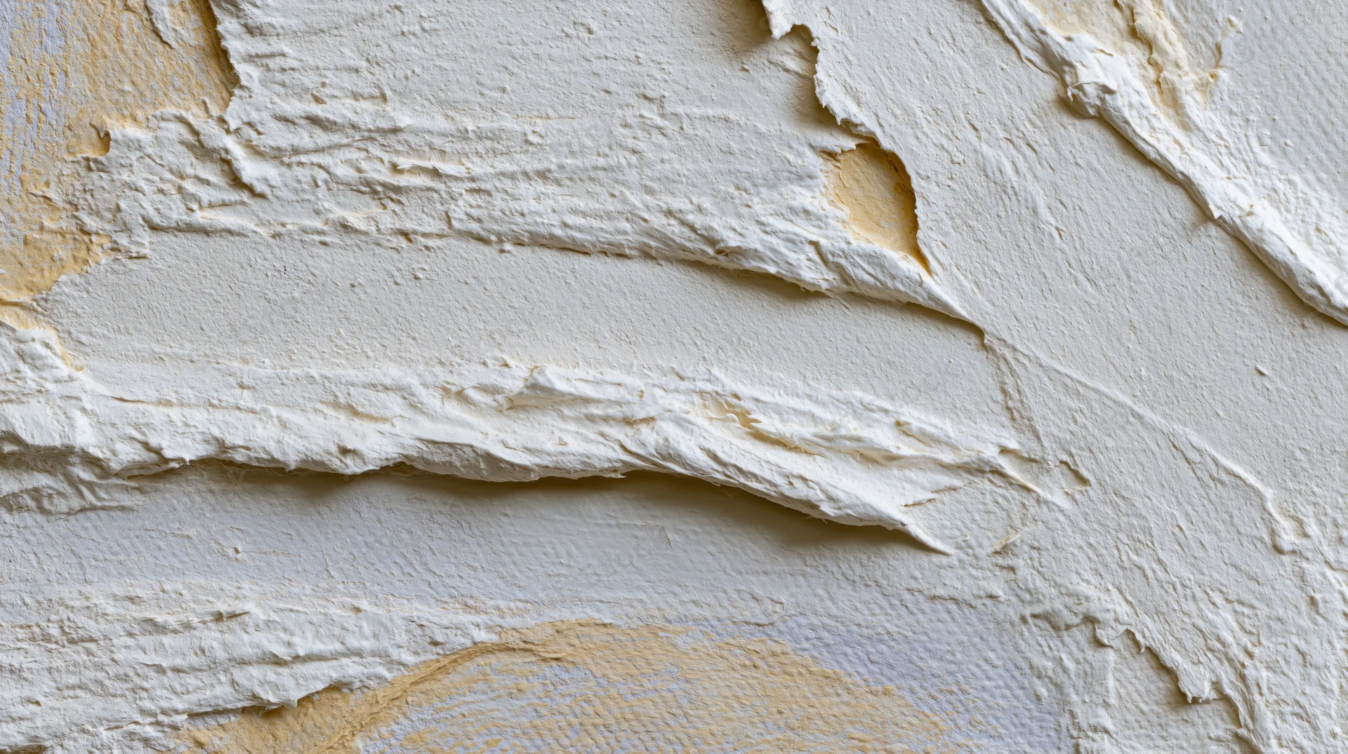 Damaged white plaster wall with peeling paint and repair patches showing beige underlayer