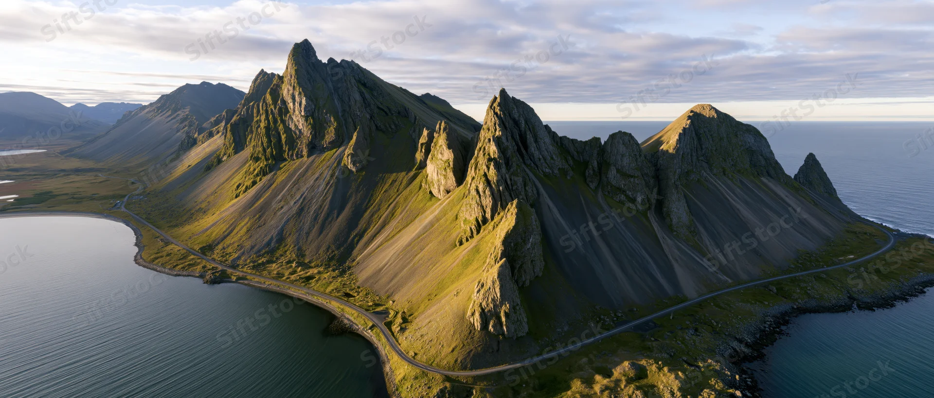 Rugged mountain peaks along a winding coastal road by the sea at sunset