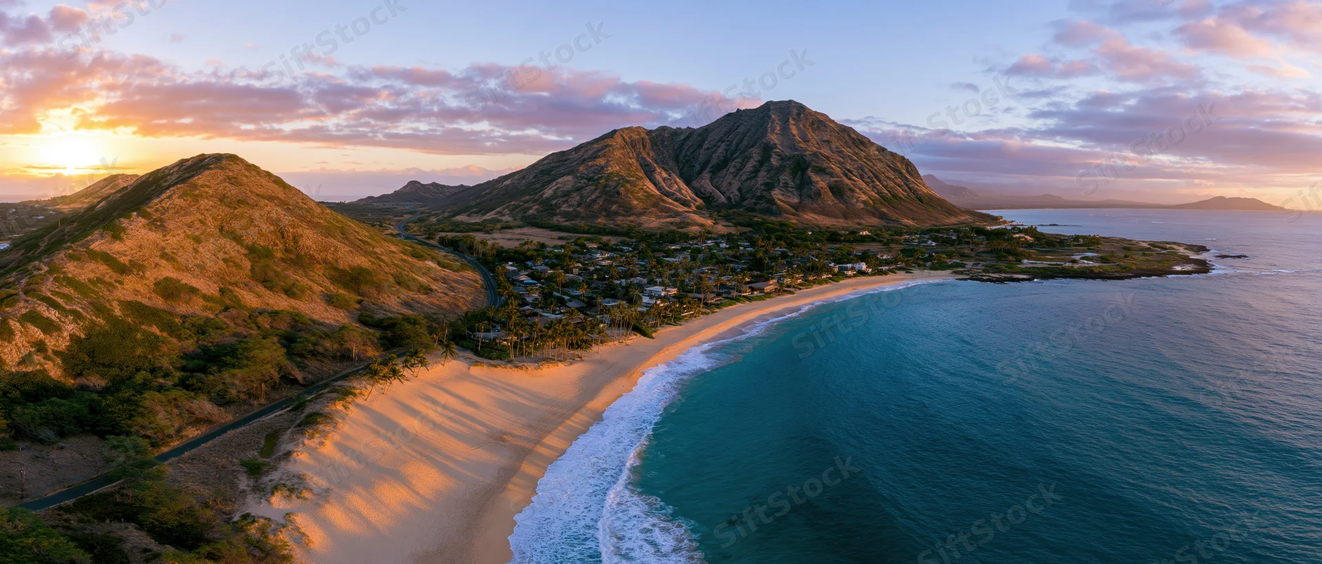 Aerial view of a tropical beach with waves crashing along the shore at sunset near Diamond Head mountain in Hawaii