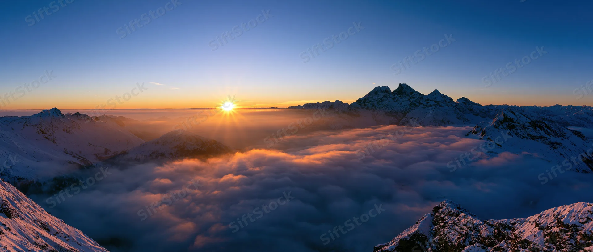 Snow-covered mountain peaks rising above a sea of clouds at sunrise