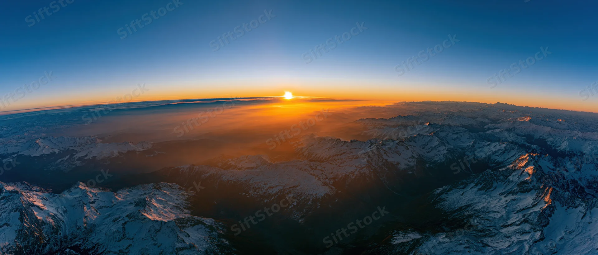 Snow-covered mountain peaks at sunrise viewed from above the clouds