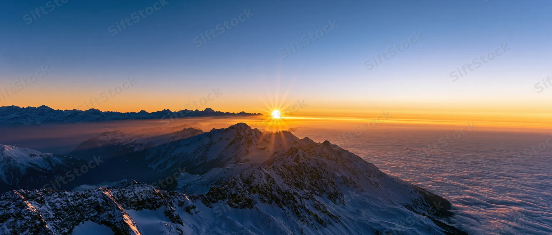 Snow-covered mountain peaks at sunrise above a sea of clouds