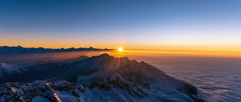 Snow-covered mountain peaks at sunrise above a sea of clouds
