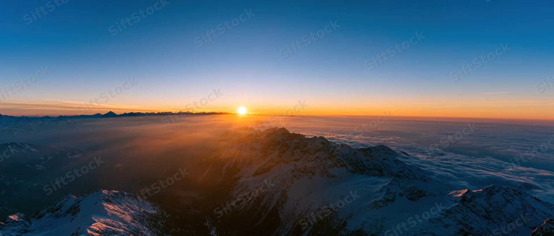 Snow-covered mountain peaks rising above a sea of clouds at sunrise